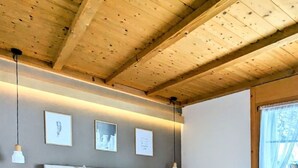 A bedroom with a large bed, wooden ceiling beams, and a window with a view of trees. - Margrit West by Interhome (Lauterbrunnen)