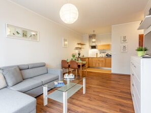 A modern living room with a grey sofa, a glass coffee table, and a dining area with wooden chairs and a kitchen in the background. - Apartment Verde in Swinemünde by Interhome (Swinoujscie)