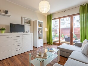 A modern living room with a sofa, a glass coffee table, a TV, a bookshelf, and a sliding glass door to an outdoor area. - Apartment Verde in Swinemünde by Interhome (Swinoujscie)