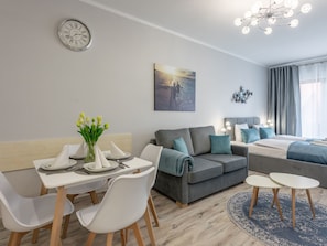 A modern living room with a dining area, a gray sofa, a bed, and a clock on the wall. - Kormoran 10 by Interhome (Swinoujscie)