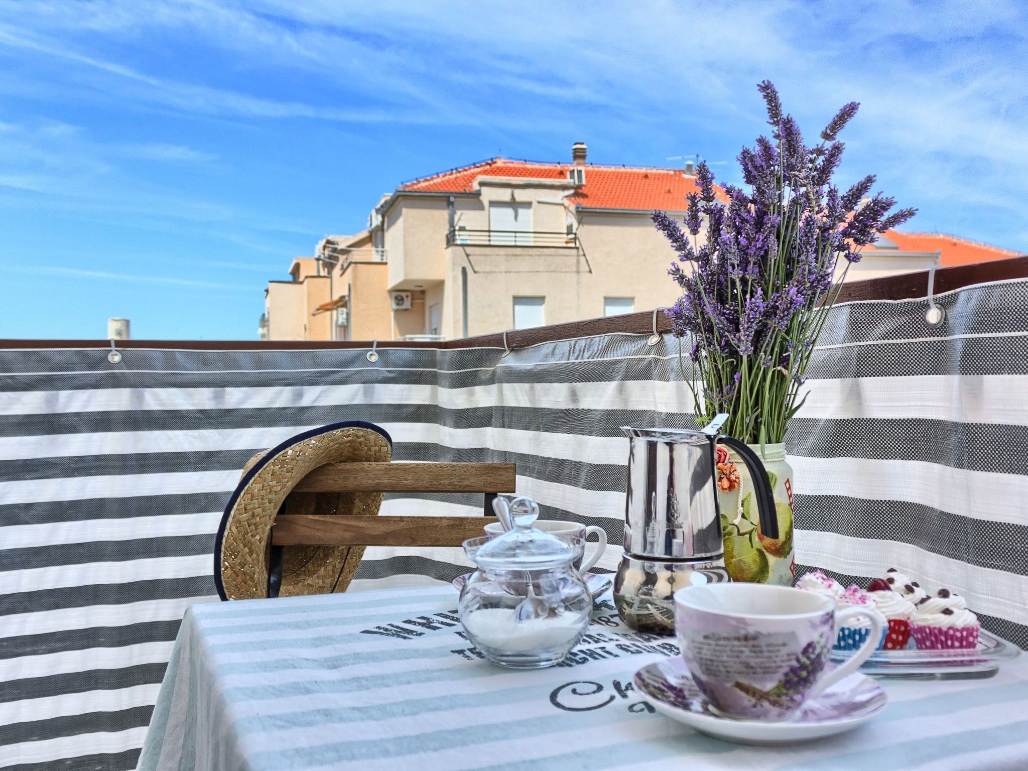 A table set with a teapot, sugar bowl, cups, and a vase of lavender.