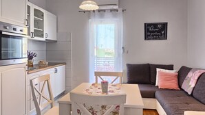 Ein kompakter Wohnbereich mit Küchenzeile, einem Esstisch mit Stühlen, einer Couch und einem dekorativen Wandbild.