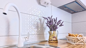 Eine Küche mit einer Spüle aus Edelstahl, einem weißen Wasserhahn, einer Vase mit violetten Blumen und einem Brotkorb auf der Arbeitsfläche.