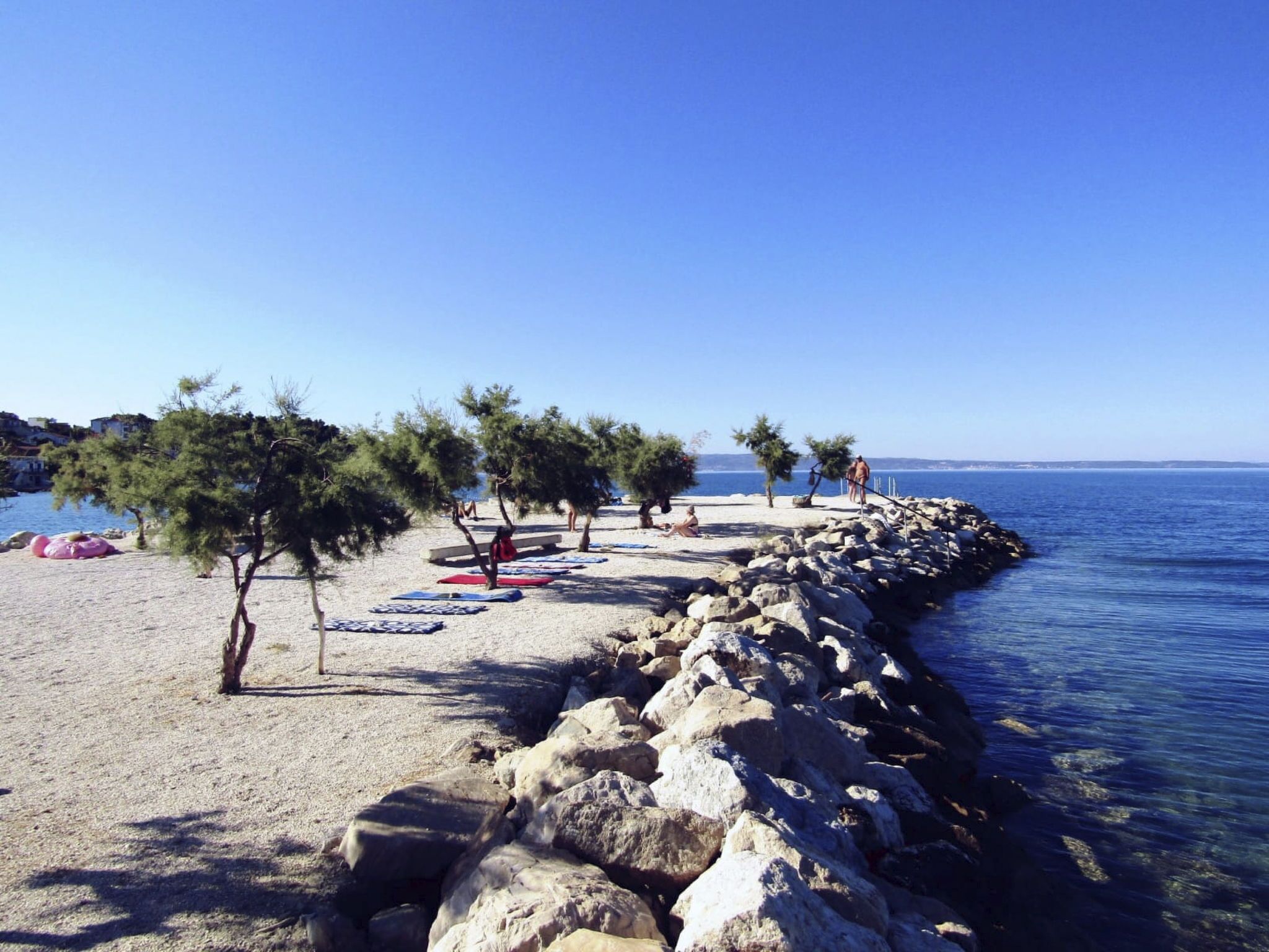 Ein Strand mit blauem Himmel, felsigem Ufer und Bäumen.