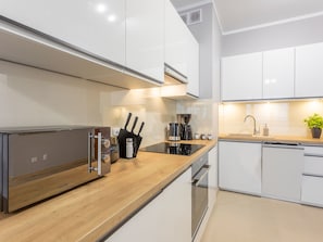 Eine moderne Küche mit weißen Schränken, einer Holzarbeitsplatte, einem eingebauten Backofen, einer Kaffeemaschine und einem Toaster.