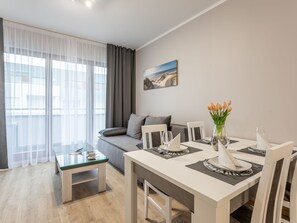 Ein modernes Wohnzimmer mit einem Glastisch, einem grauen Sofa und einem Essbereich mit einem weißen Tisch für zwei Personen.