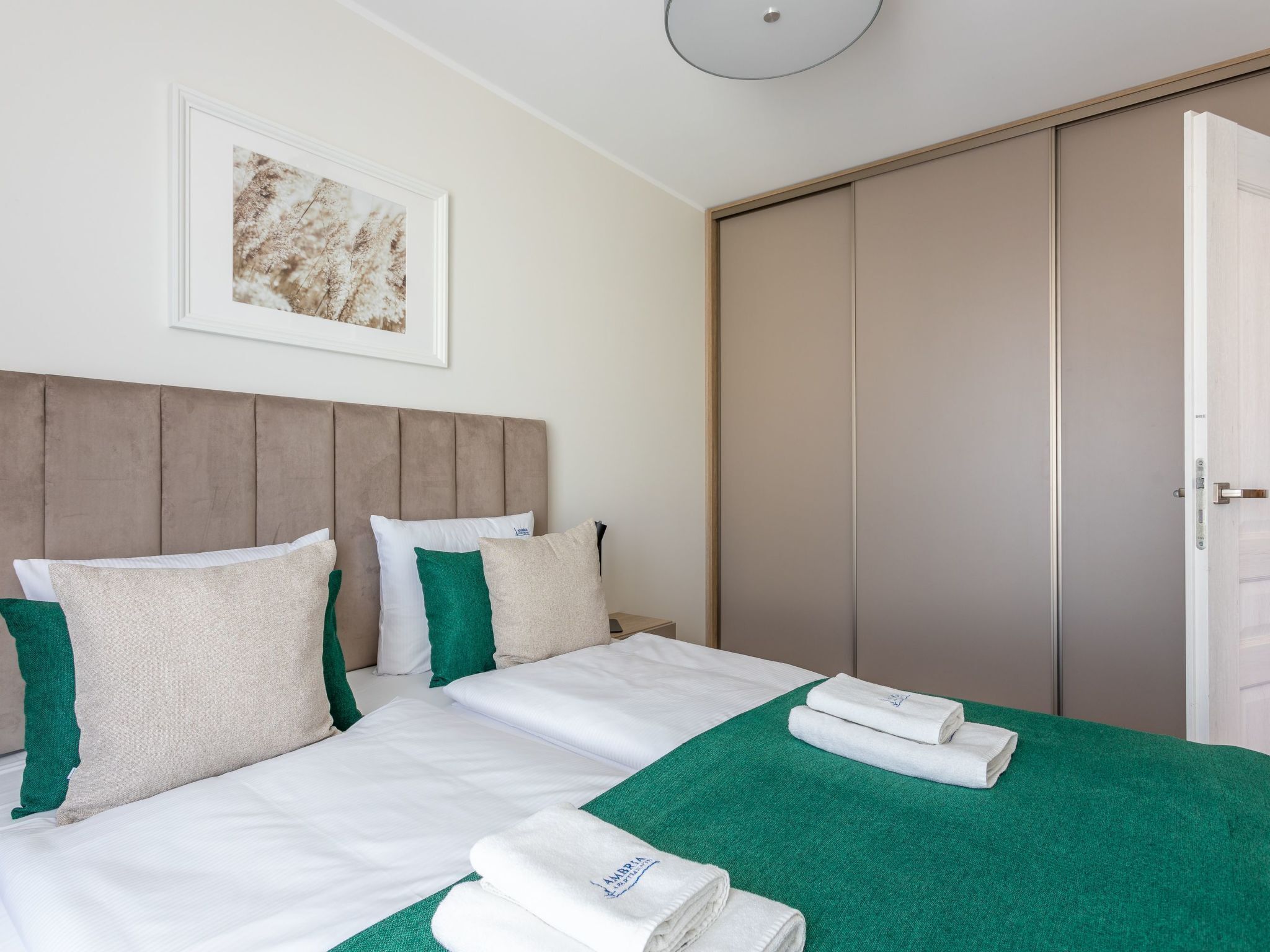 A hotel room with a bed, pillows, a green towel, and a framed picture on the wall.