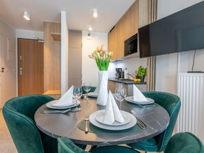 A dining area with a round table set for four, green upholstered chairs, a vase with flowers, and a kitchen in the background. - mit toller Aussicht in Swinemünde by Interhome (Swinoujscie)