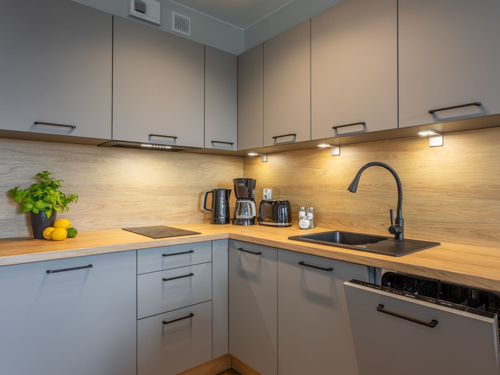 A modern kitchen with grey cabinets, a wooden countertop, a black faucet, and a coffee maker.