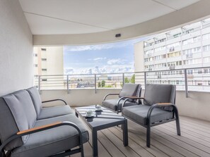 Ein Balkon mit grauen Polsterstühlen, einem kleinen Tisch und Blick auf eine Stadtlandschaft.