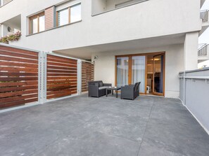 Eine moderne Außenpatio mit grauen Fliesen, einem Holzzaun und einer Glastür, die auf einen Balkon führt.
