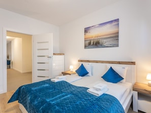 Ein Schlafzimmer mit einem Bett, einem Nachttisch, einem Wandbild und einer Tür zu einem anderen Raum.