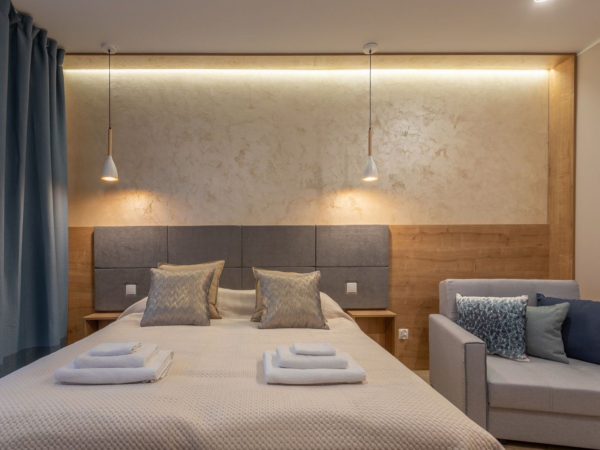 Una habitación de hotel moderna con una cama grande, dos mesitas de noche, un sofá y una pared con textura.