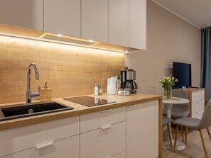 A modern kitchen with a sink, stove, and coffee maker. There is a dining area with a table and chairs. - Elegante Ferienwohnung Dune 734 by Interhome (Swinoujscie)