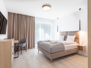 Ein modernes Hotelzimmer mit Bett, Nachttisch, Lampe, Schreibtisch, Stuhl und großem Fenster mit Vorhängen.