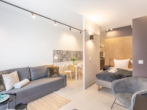 A modern, well-lit living room with a grey sofa, a small round table, and a bed with a headboard. - Kormoran in modernem Appartementhaus by Interhome (Swinoujscie)