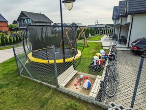 A fenced trampoline area with a basketball court, bicycles, and a car parked nearby. - Haus 1 in Sarbinowo by Interhome (Sarbinowo)