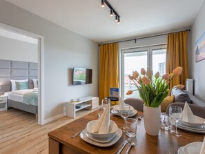 A modern hotel room with a neatly made bed, a flat-screen TV mounted on the wall, a dining area with a table set for two, and a window with curtains. - Urlaub auf Usedom, Apartment Sun Towers A46 by Interhome (Swinoujscie)