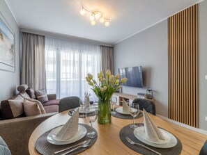 A modern dining area with a wooden table set for four, a vase of flowers, and a television in the background. - Apartment Maja by Interhome (Swinoujscie)