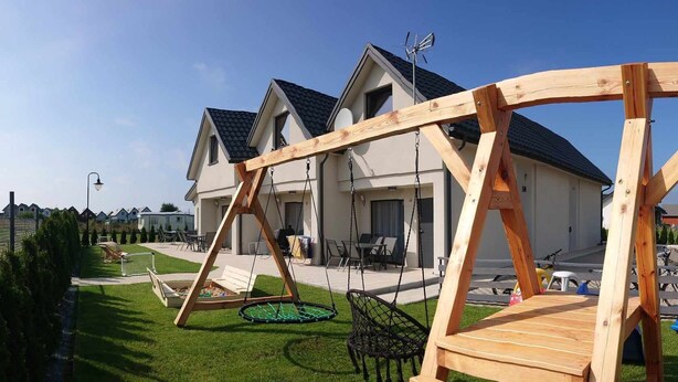Um conjunto de baloiços de madeira numa zona residencial, com casas ao fundo.