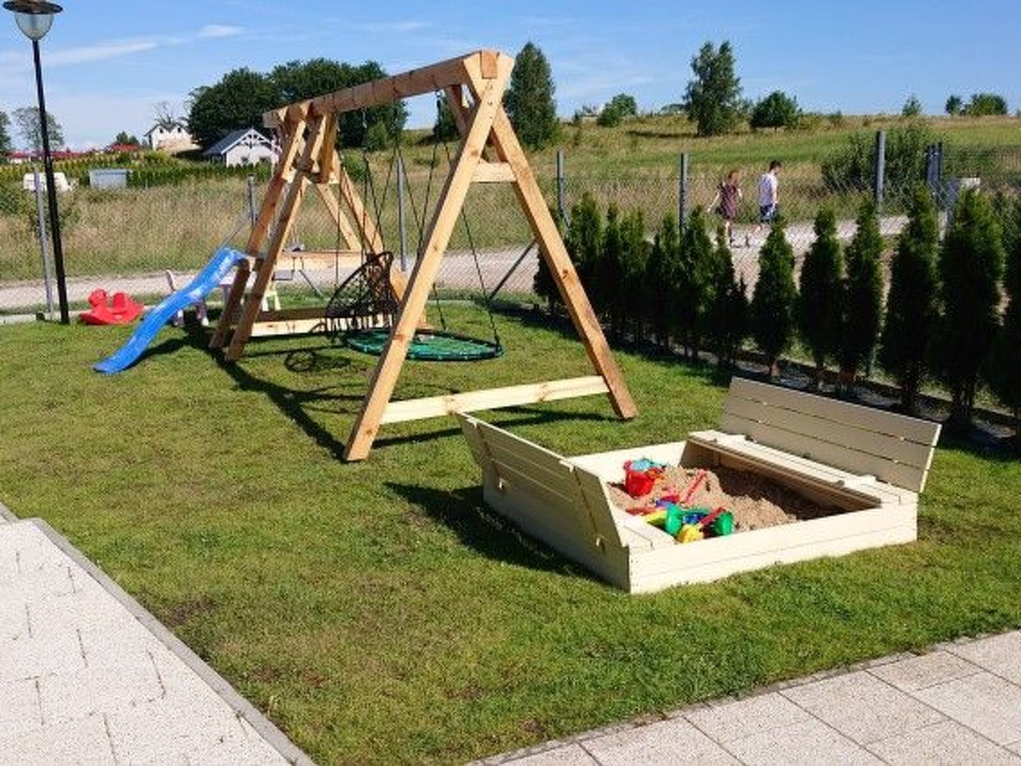 A playground with a swing set and a slide, a sandbox with toys, and a grassy area.