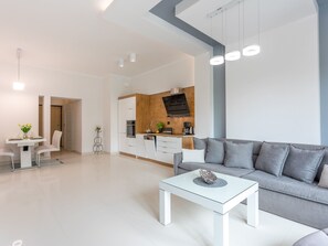 A modern living room with a glass coffee table, grey sofa, and a kitchen area with wooden accents. - Geräumiges und luxuriöses Appartement Tower 12 by Interhome (Swinoujscie)
