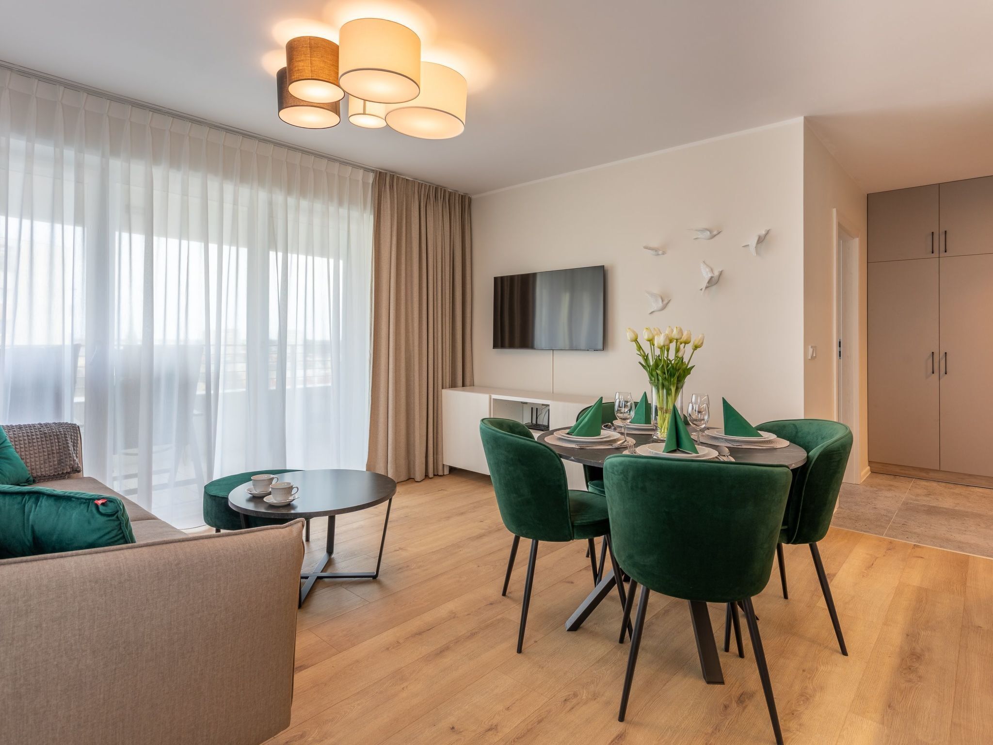 A modern living room with a sofa, a dining table set for four, and a TV mounted on the wall.