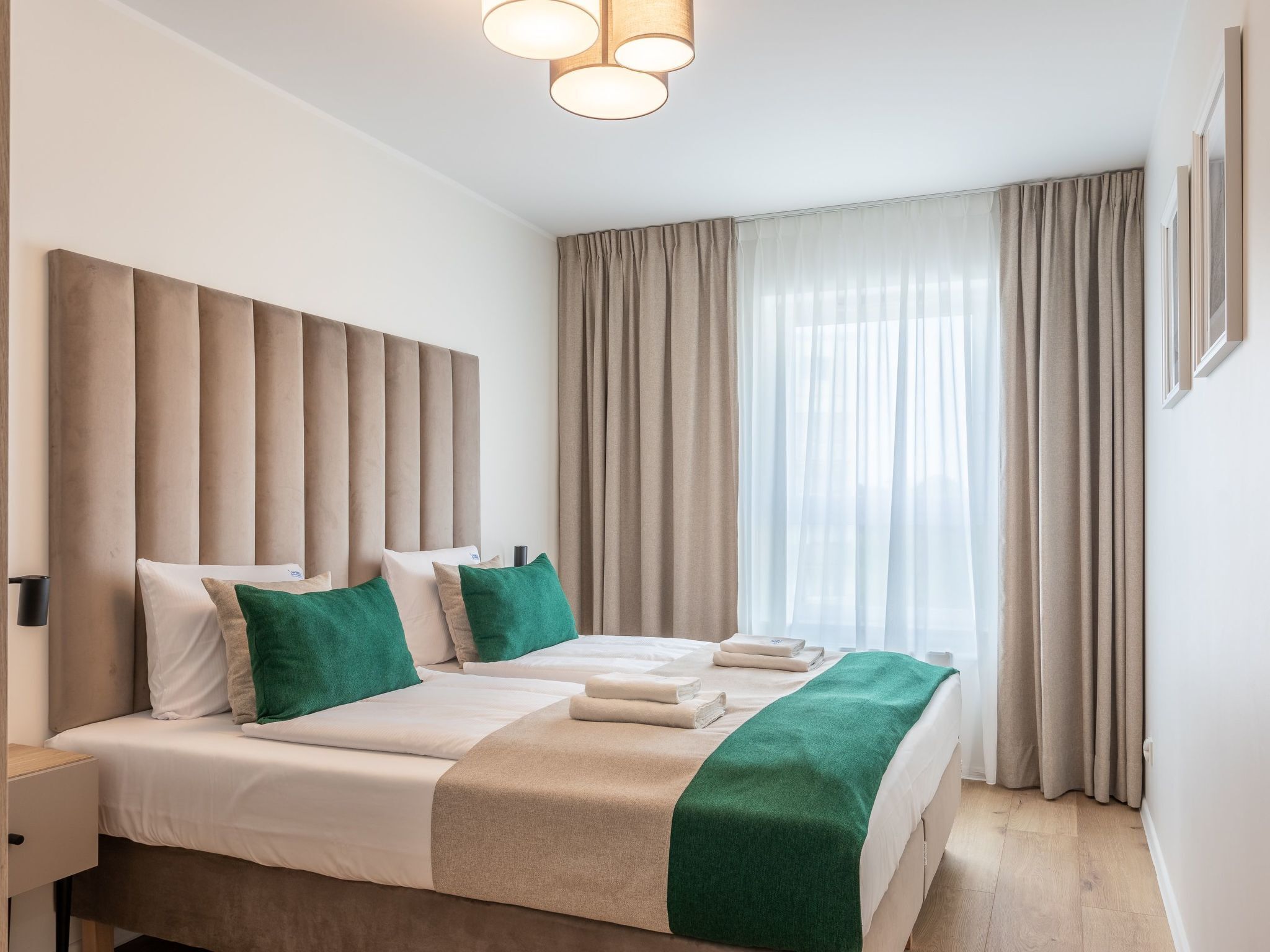 Ein modernes Hotelzimmer mit einem großen Bett, beigefarbenen Vorhängen und Blick auf die Stadt.