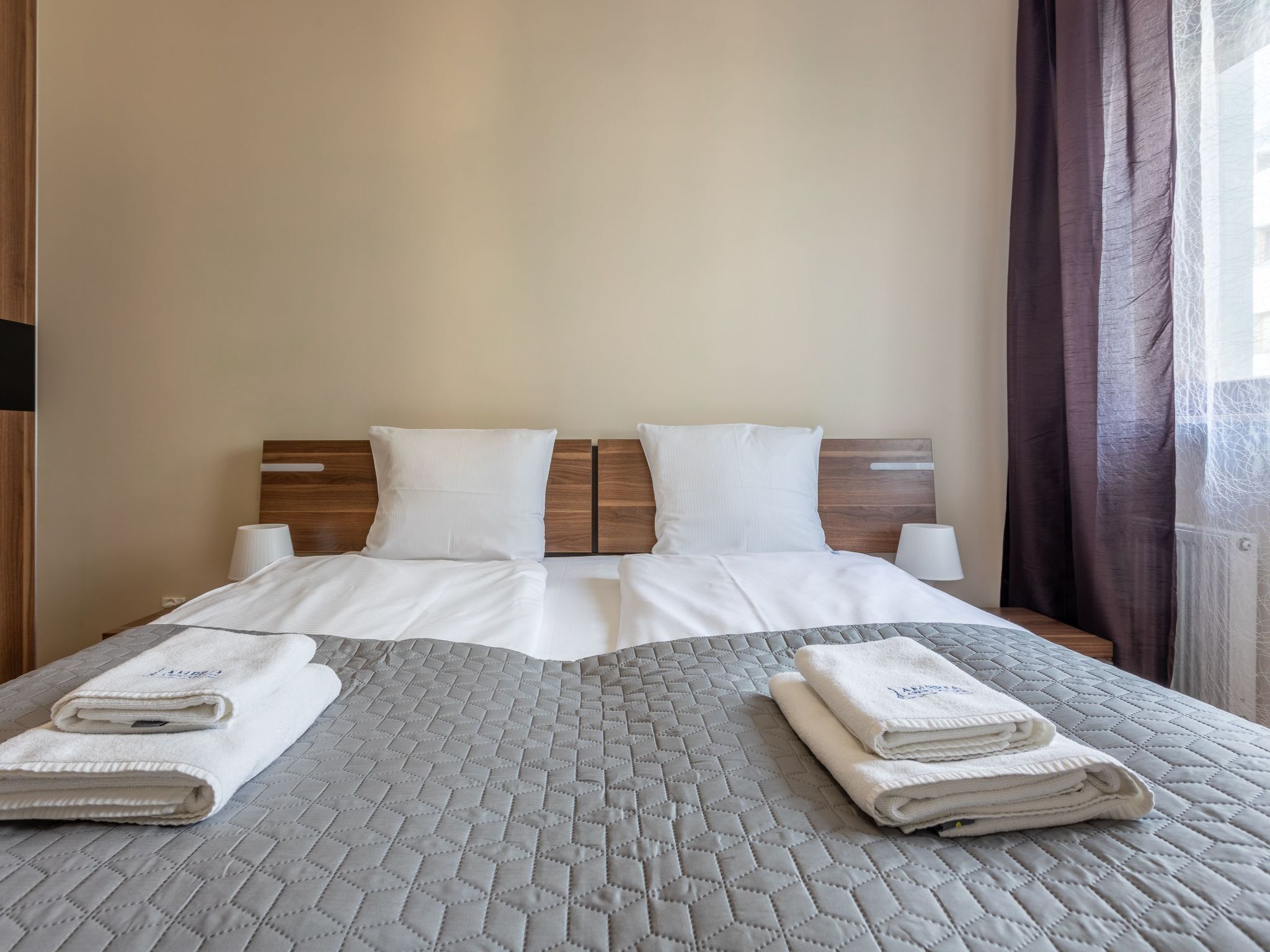 Un lit double avec une couvre-lit matelassée grise, deux oreillers blancs et deux serviettes blanches pliées posées sur le lit.