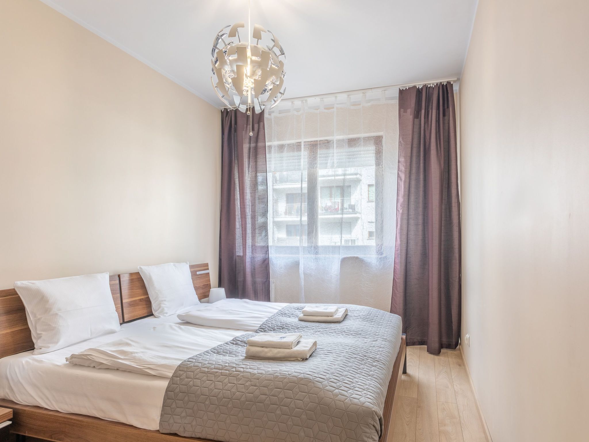 A neatly made bed with a quilted blanket, a wooden headboard, and a hanging light fixture.