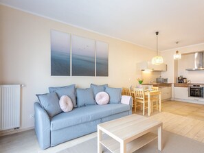 A modern living room with a sofa, a coffee table, and a dining area with a table and chairs. There is a kitchen area with a stove and a hanging light fixture. - Charmante Ferienwohnung Sand auf Usedom by Interhome (Swinoujscie)