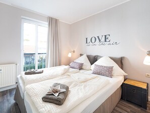 A double bed with a star-shaped pillow, two bedside tables, a wall with a 'LOVE is in the air' sign, and a window with curtains. - Villa Buskam Wohnung Picasso by Interhome (Baabe)
