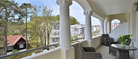 Ein Balkon mit Korbmöbeln, einem Glastisch und einem Blumenstrauß.