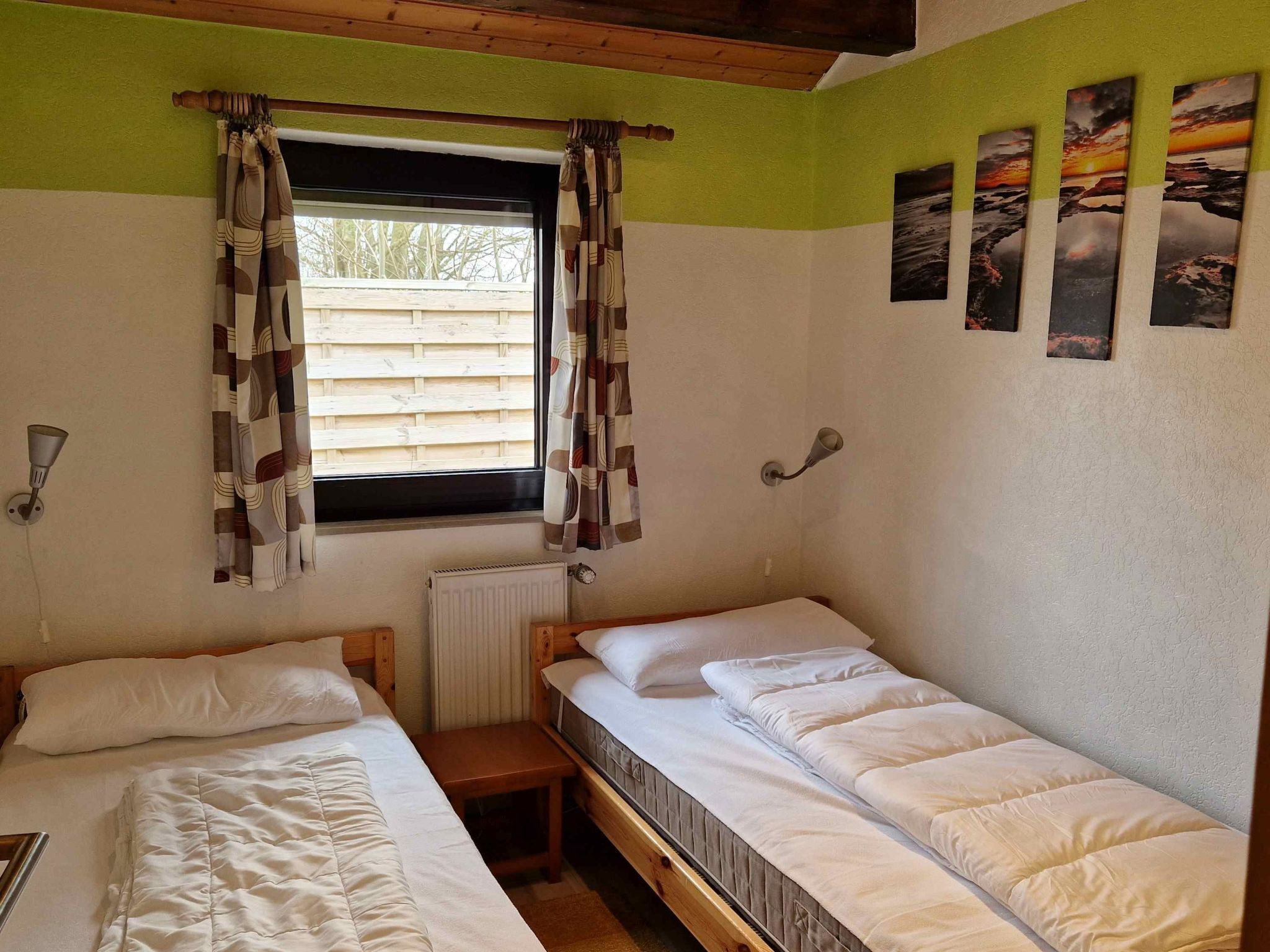 Une chambre avec deux lits simples, une fenêtre avec des rideaux, un radiateur et des appliques murales.