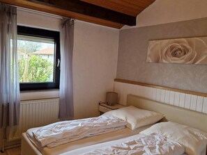 Ein Schlafzimmer mit Bett, Nachttisch, einem Fenster mit Vorhängen und einer Wanddekoration mit Rosen.