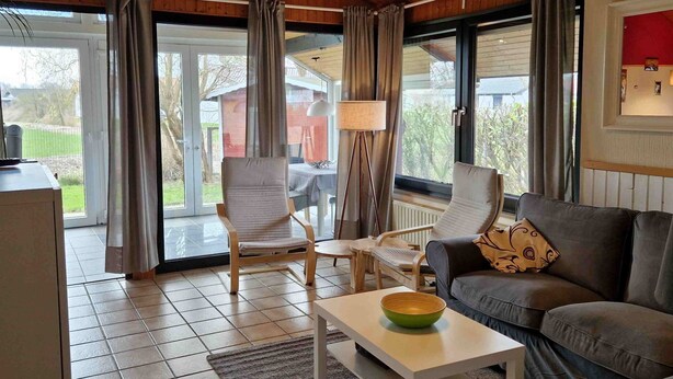 Ett mysigt vardagsrum med ett träpanelat tak, en soffa, två fåtöljer, ett soffbord med en skål på och en golvlampa.