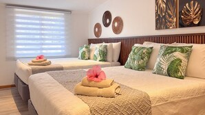 Habitació d'hotel amb dos llits, cadascun amb una tovallola enrotllada i una flor rosa. Hi ha almoinades i decoració mural amb motius de fulles tropicals i dibuixos circulars.