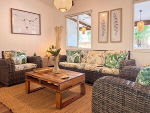 Una sala de estar acogedora con muebles de mimbre, una mesa de centro de madera y cojines con motivos tropicales.