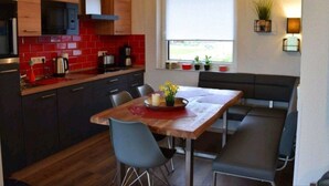 A compact kitchen with wooden cabinets, a red-tiled backsplash, a dining table with chairs, and a bench. - Vacation home  by Interhome (Burhave)