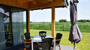 A covered outdoor dining area with a table and chairs, a pergola overhead, and a view of a green field. - Vacation home  by Interhome (Burhave)