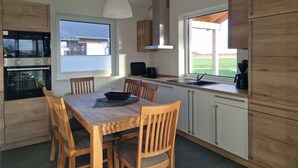 A modern kitchen with wooden cabinets, a dining table, and chairs. - G28 Eingezäuntes Ferienhaus mit Infrarotkabine by Interhome (Burhave)