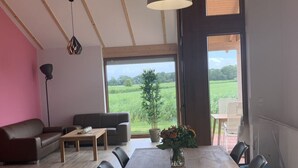 A dining area with a wooden table, chairs, and a vase of flowers. There is a sofa and a lamp in the background. - G9 eingezäuntes Haus in Randlage mit Weitblick by Interhome (Burhave)