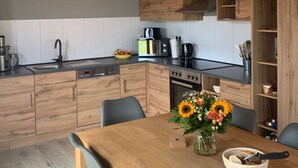 A modern kitchen with wooden cabinets, a black countertop, and a dining area with a wooden table and chairs. - G9 eingezäuntes Haus in Randlage mit Weitblick by Interhome (Burhave)