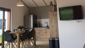 A modern kitchen with a built-in refrigerator, a dining area with a wooden table and chairs, and a mounted flat-screen TV. - G9 eingezäuntes Haus in Randlage mit Weitblick by Interhome (Burhave)