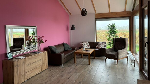 A modern living room with a pink wall, wooden furniture, and a large window offering a view of a field. - G9 eingezäuntes Haus in Randlage mit Weitblick by Interhome (Burhave)