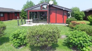 En rød bygning med parabolantenne, glasdør og en lille terrasse med et bord og stole.