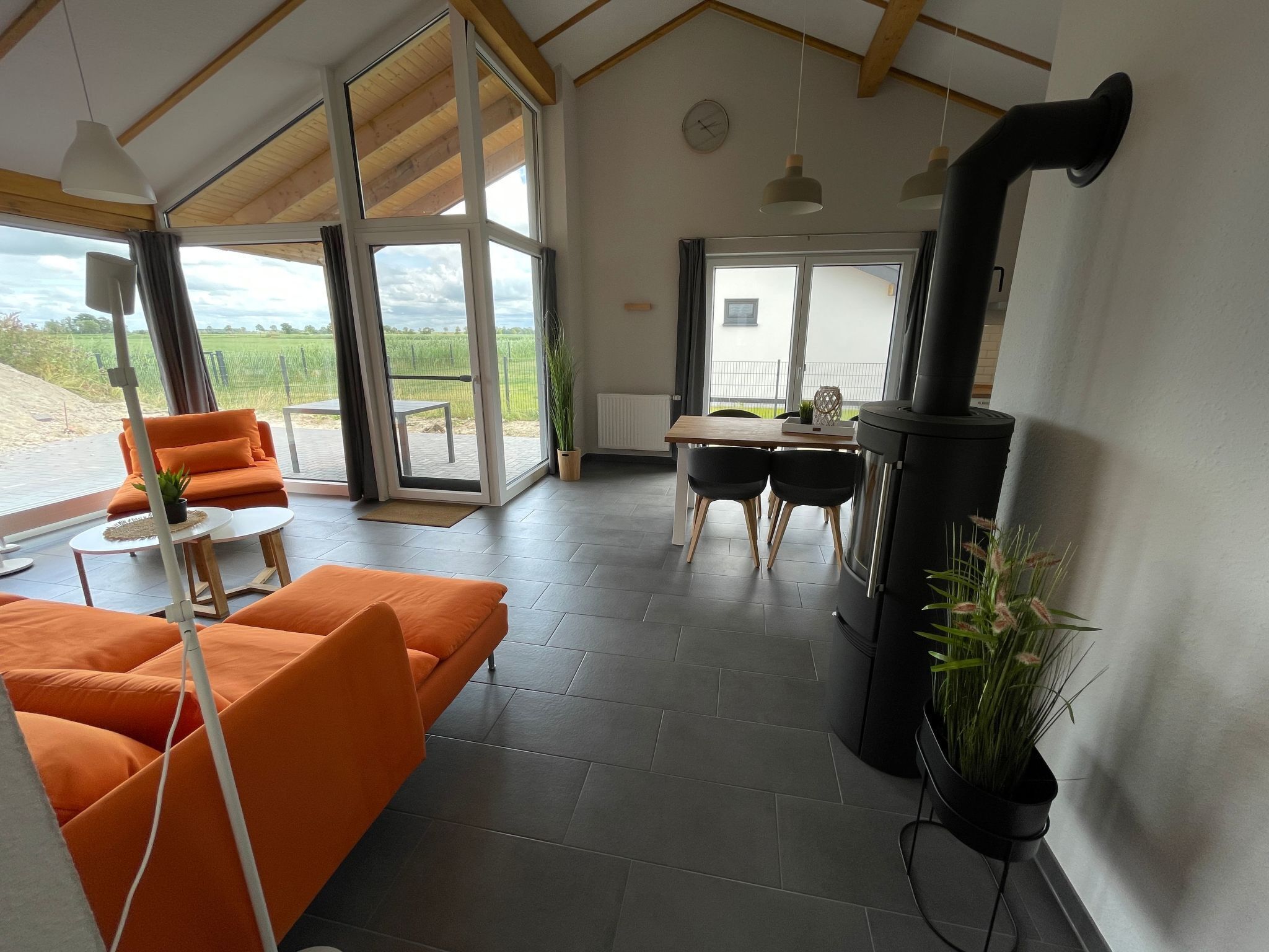 Ein modernes Interieur mit großzügigem Raumangebot, Kamin, orangenen Sitzmöbeln und großen Fenstern mit Blick ins Freie.