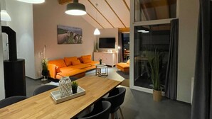 Een moderne woonkamer met een houten eettafel, een oranje bank en een groot raam.