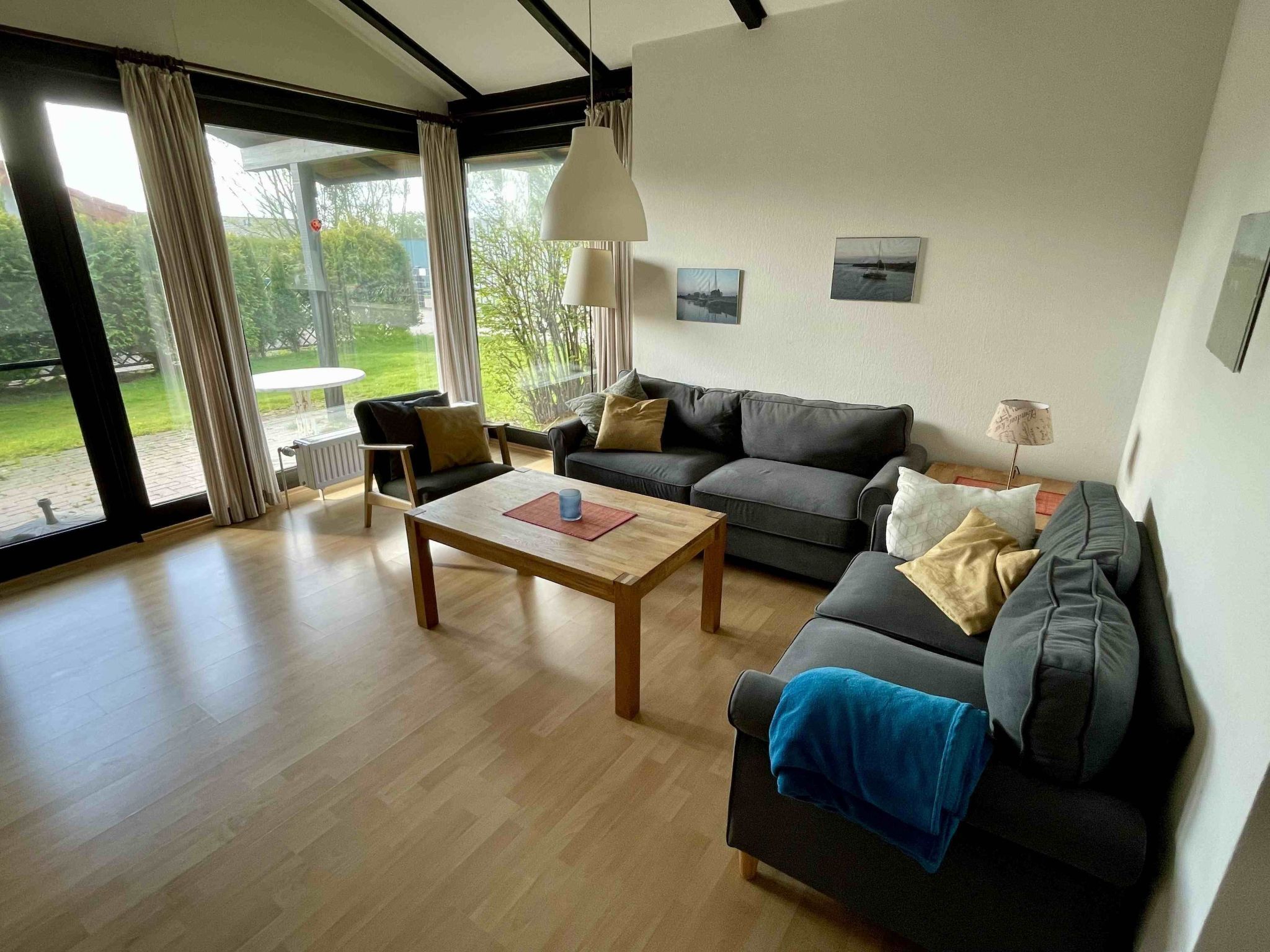 A modern living room with a sofa, coffee table, and a view of a garden through large windows.