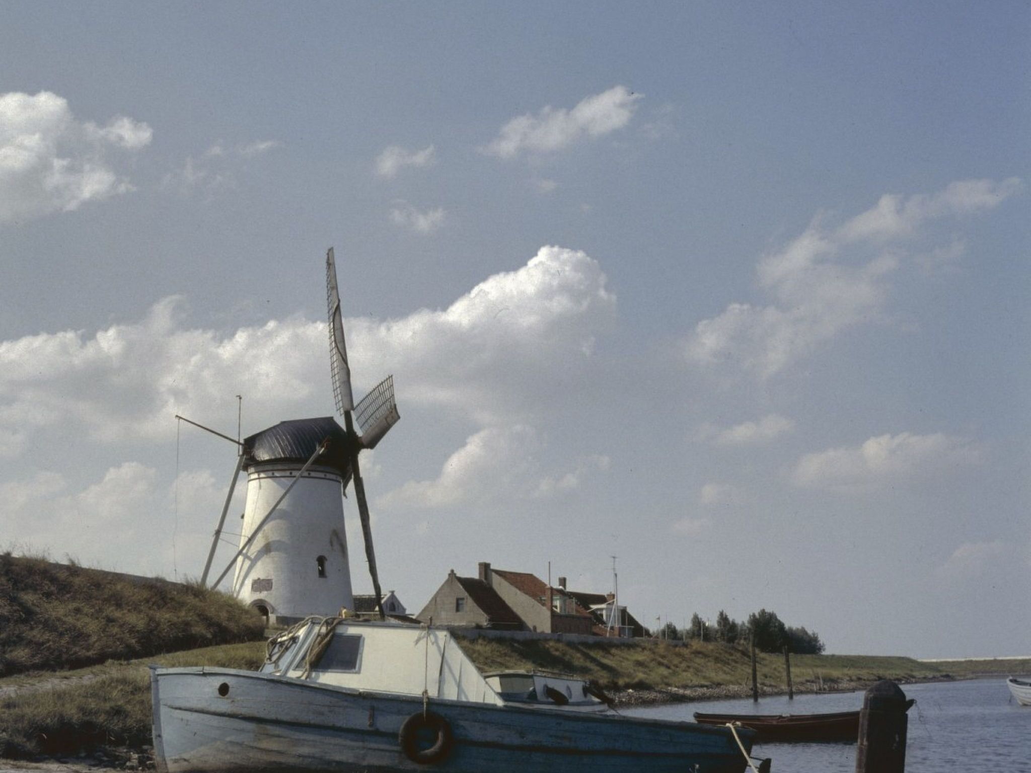 Un molino, un bote y un edificio junto al agua.